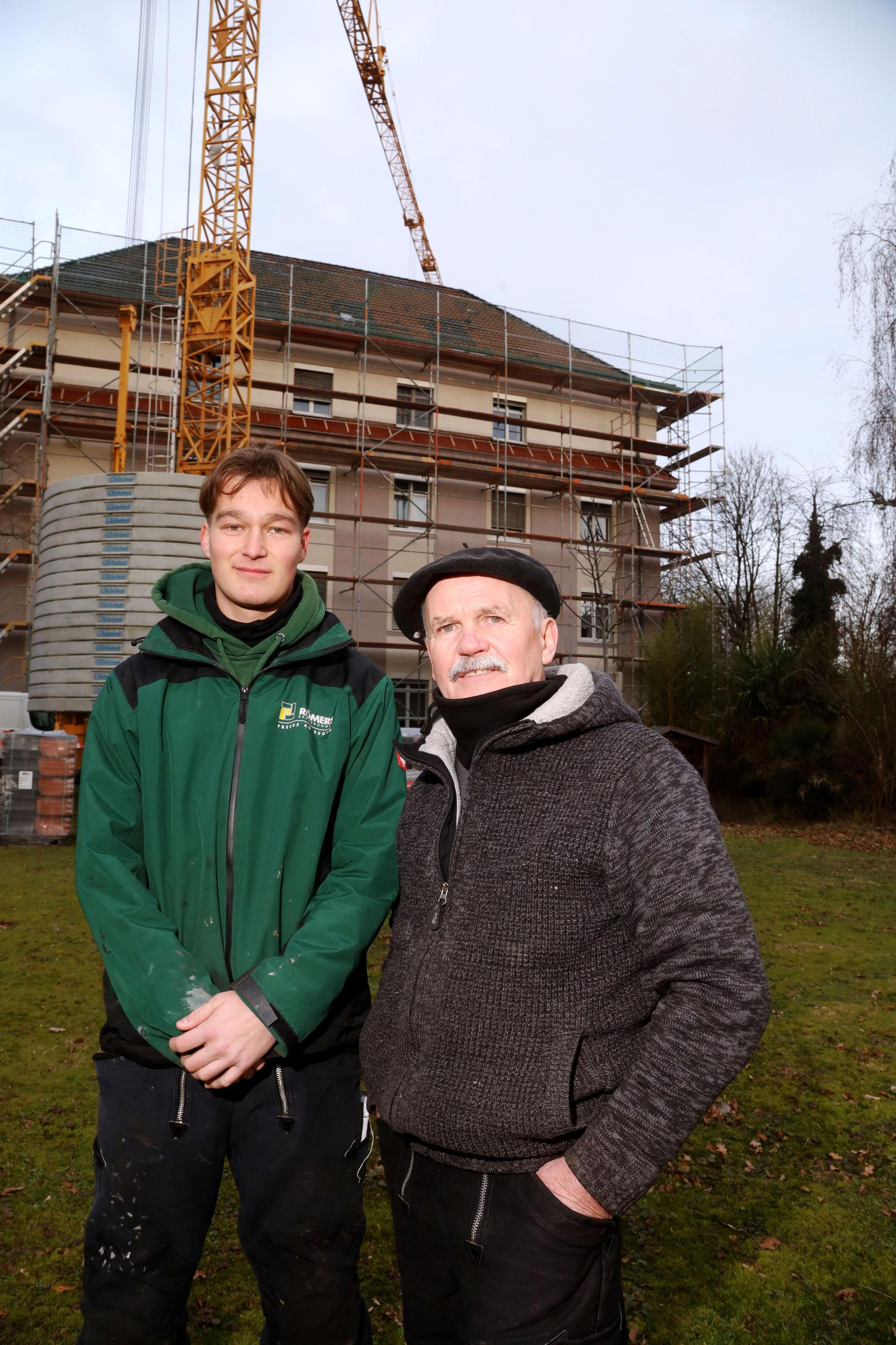 Senior-Dachdecker Bernhard Bartnik ist mit Geselle Noah Beckers zu sehen vor einem eingerüsteten Haus.