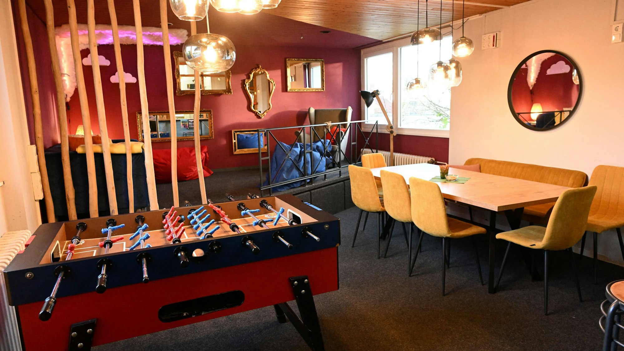 Ein Raum mit roten und orangen Wänden, einem Tischkicker und Spiegeln an den Wänden.