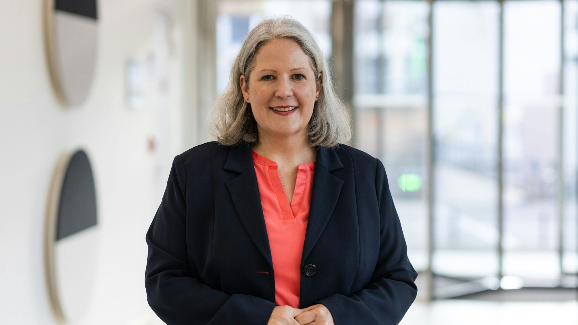 Eine Frau mit roter Bluse und schwarzem Blazer schaut in die Kamera.