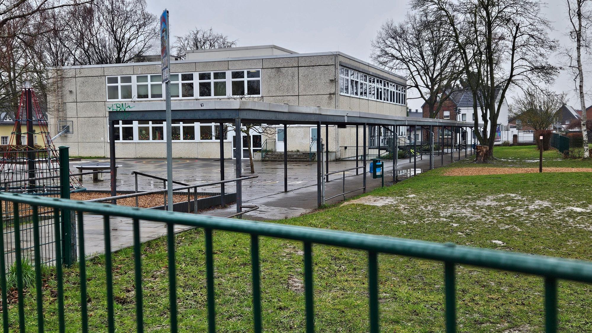 Zu sehen ist das Gebäude der Grundschule, im Vordergrund verschwommen ein grüner Zaun.