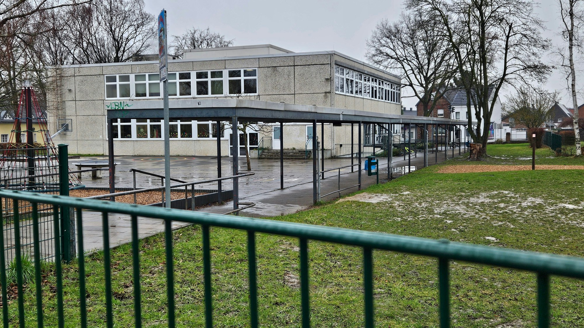 Zu sehen ist das Gebäude der Grundschule, im Vordergrund verschwommen ein grüner Zaun.