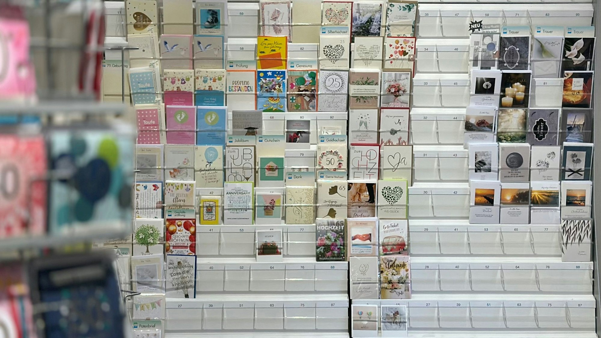 Zu sehen ist ein Regal mit Grußkarten. Links daneben steht ein Ständer, ebenfalls mit Gruß- und Glückwunschkarten.