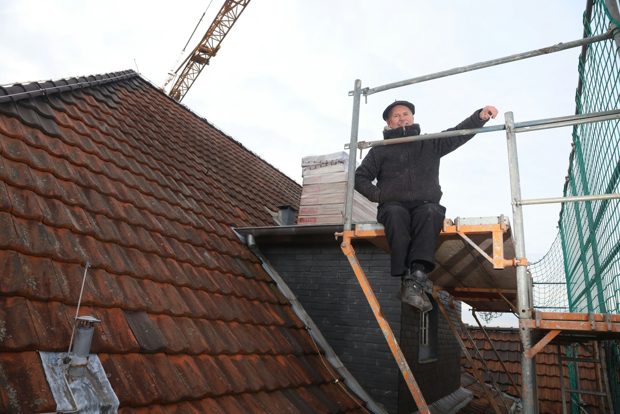 Bartnik Sitzt auf einer Gaube und lacht in die Kamera.