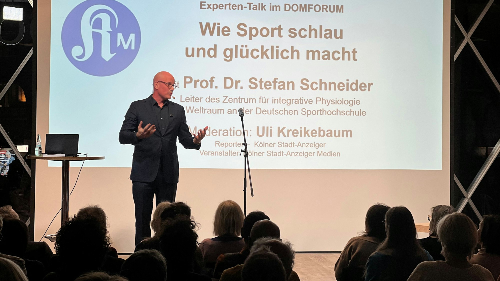 Ein Mann steht auf einer Bühne und gestikuliert.