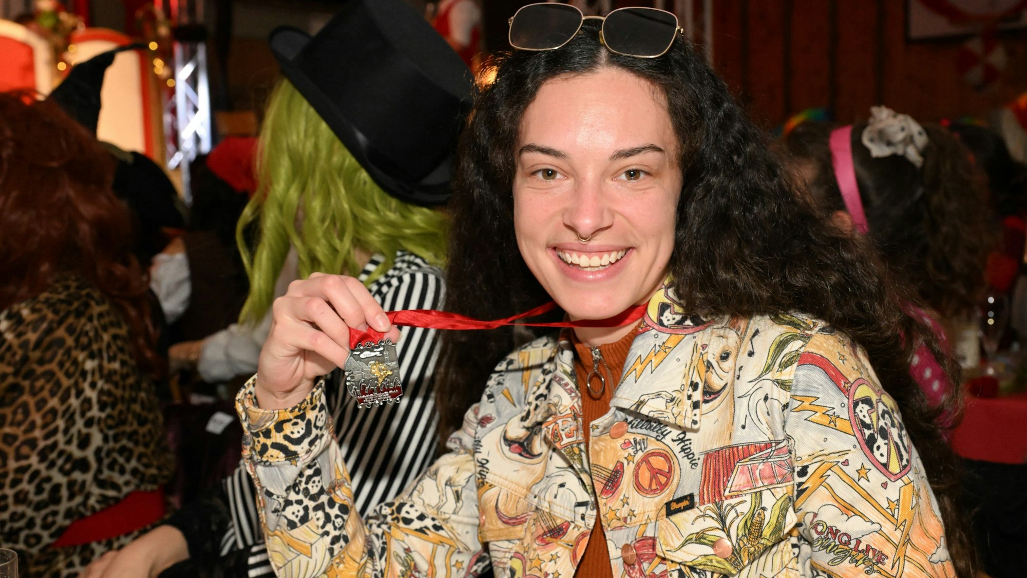 Eine Frau hat einen Karnevalsorden um den Hals und zeigt ihn lächelnd in die Kamera.