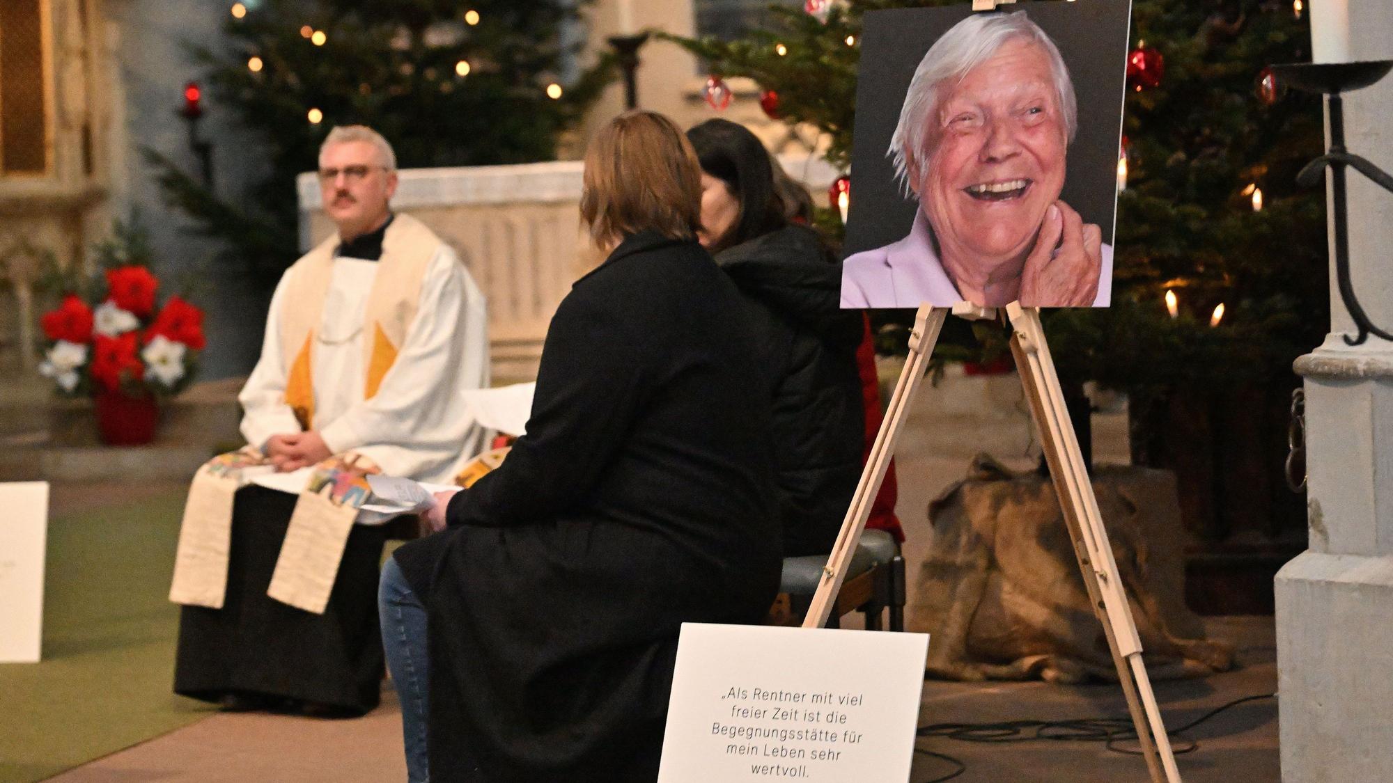 Ein katholischer Pfarrer sitzt im Altarraum einer Kirche, seitlich ist ein großes Foto aufgestellt, es zeigt das Gesicht eines lachenden Mannes.