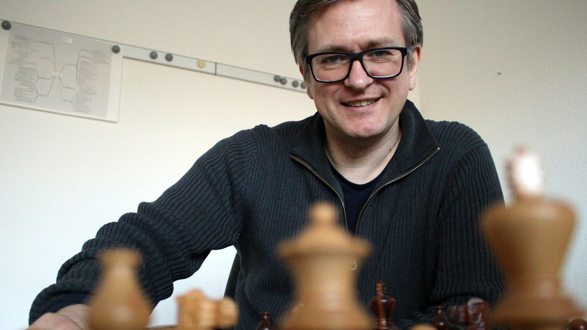Das Bild zeigt den Obengenannten an einem Schachbrett.