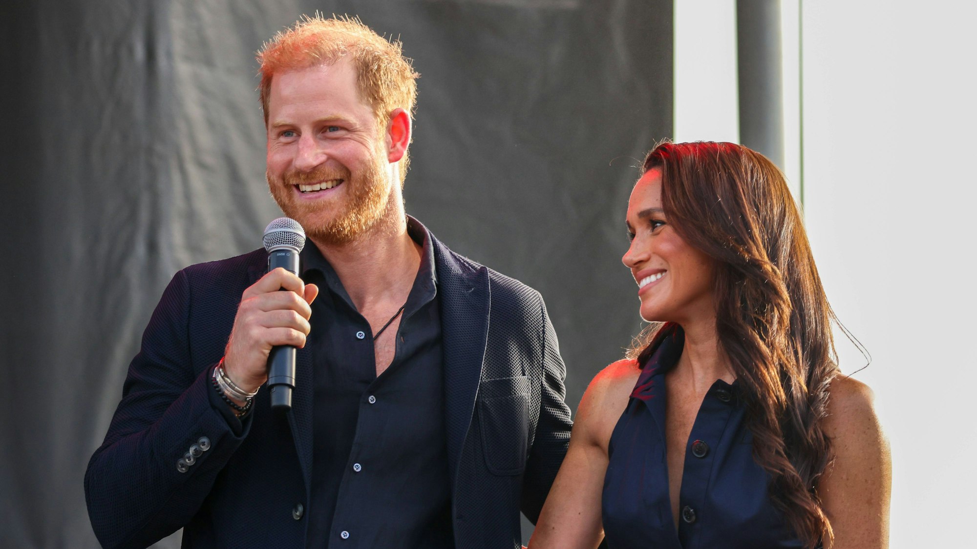 Prince Harry und Meghan Markle lächeln auf einer Bühne.