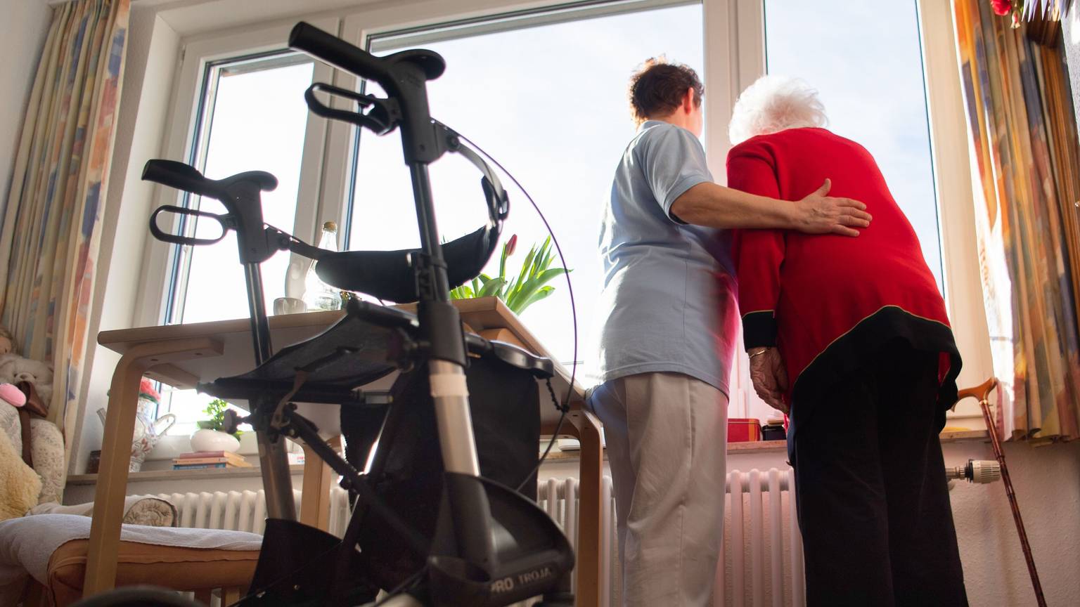 Das Bild zeigt eine Pflegerin mit einer Seniorin. Sie nimmt die ältere Frau in den Arm.