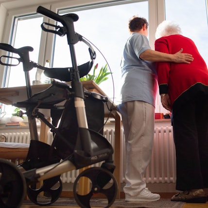 Das Bild zeigt eine Pflegerin mit einer Seniorin. Sie nimmt die ältere Frau in den Arm.