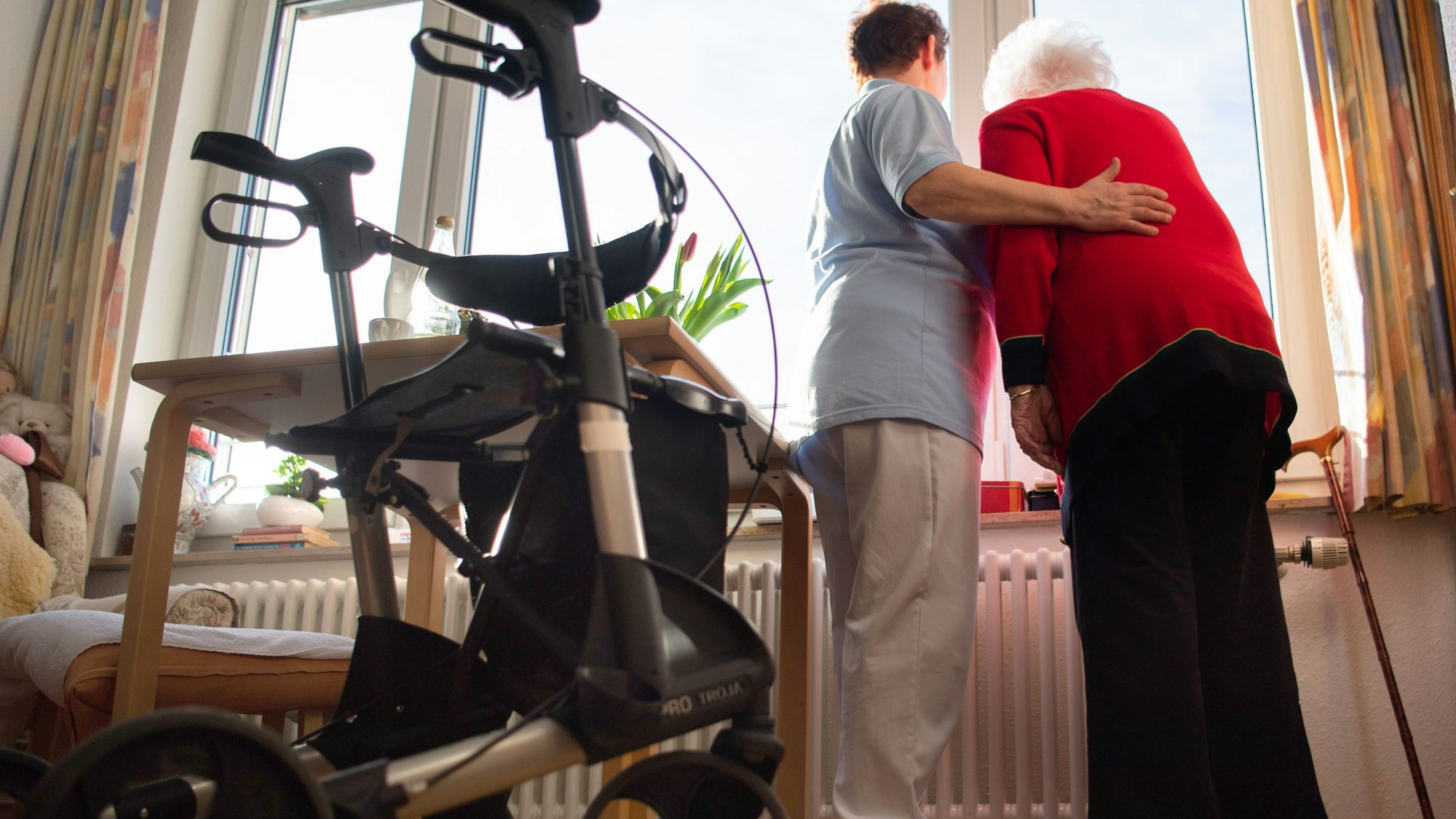 Das Bild zeigt eine Pflegerin mit einer Seniorin. Sie nimmt die ältere Frau in den Arm.