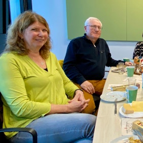 Vier Frauen und ein Mann sitzen an einem langen Frühstückstisch, auf dem Speisen und Getränke angerichtet sind.