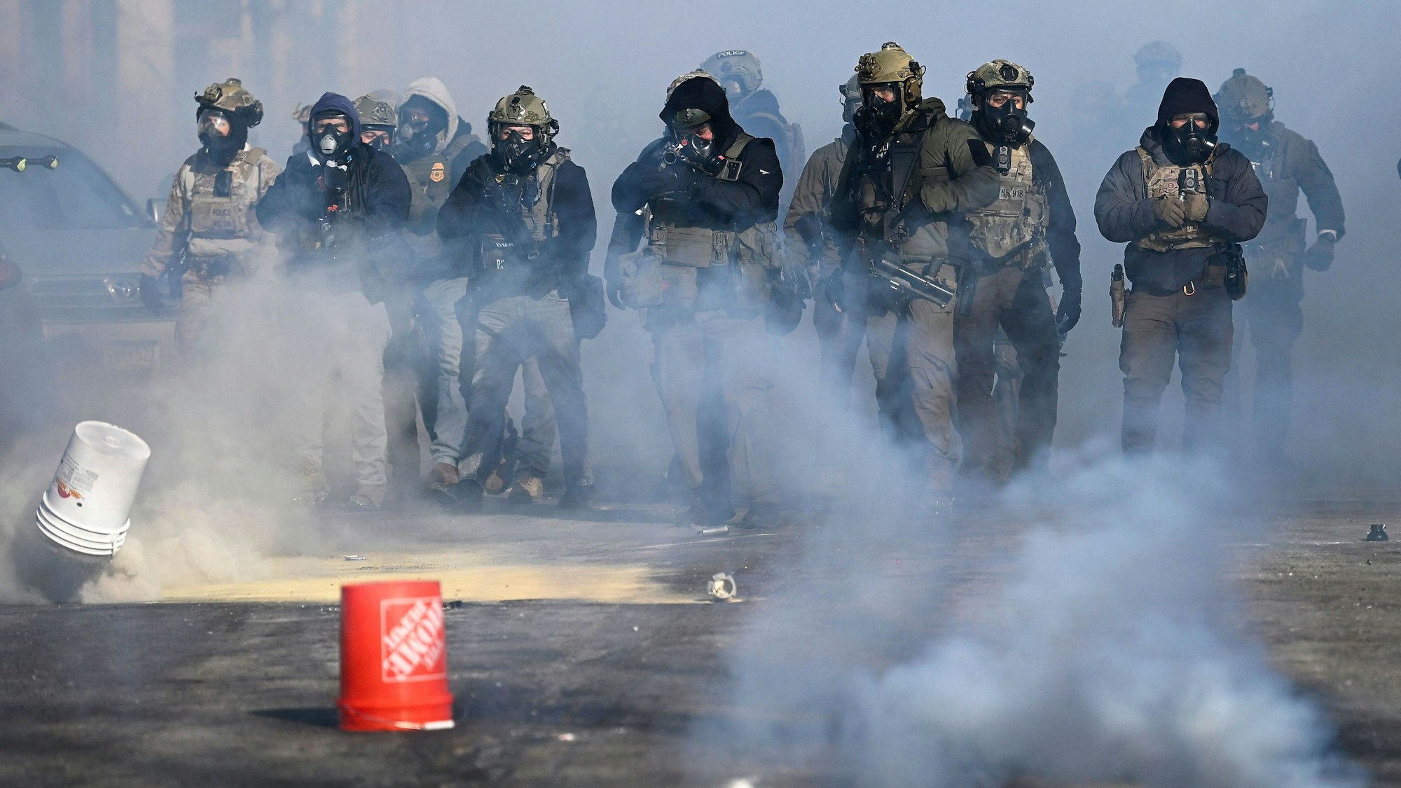 Bundesbeamte richten Waffen auf Demonstranten, während Tränengas eingesetzt wird.