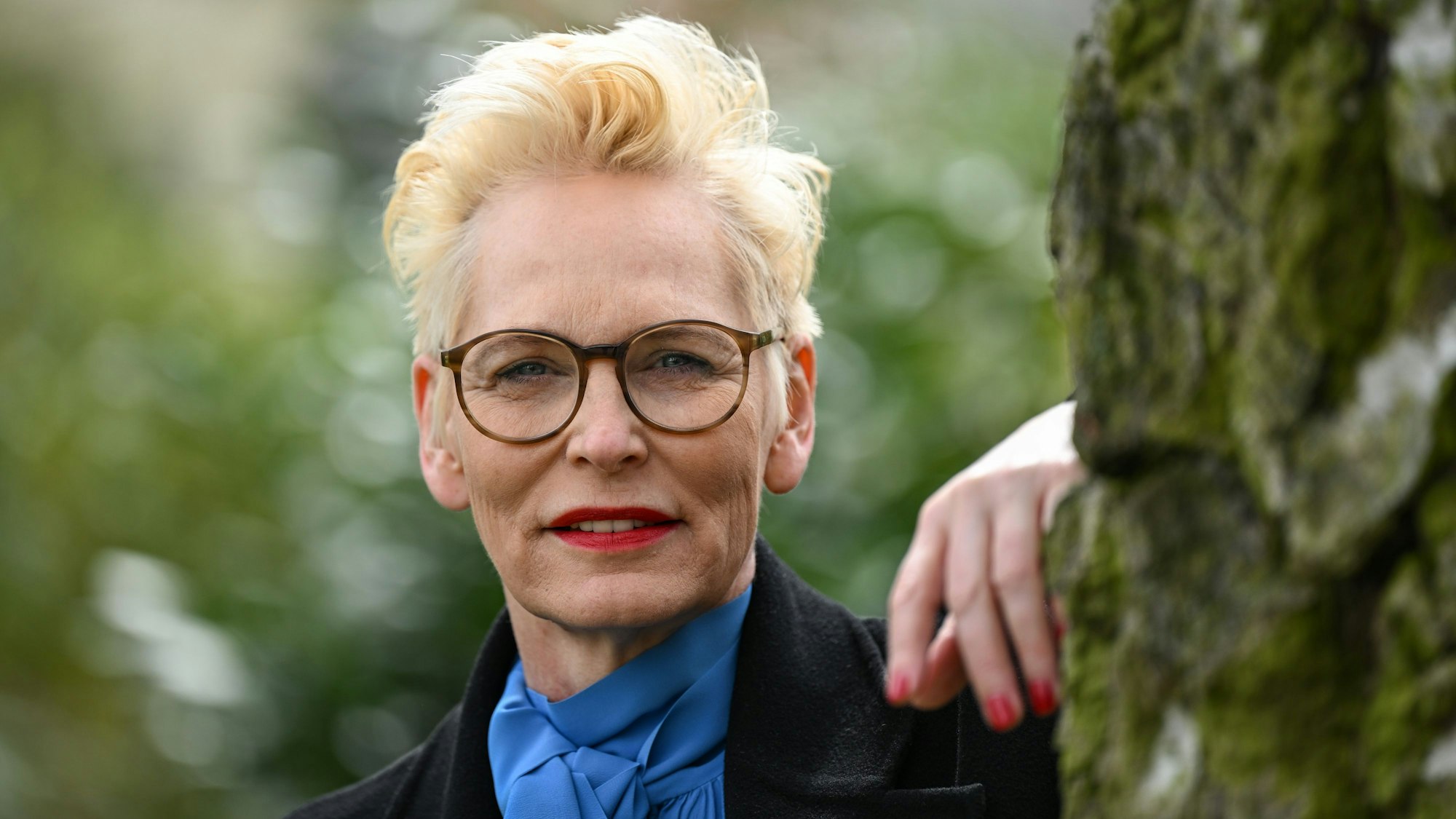 Bärbel Schäfer lehnt an einem Baum und blickt in die Kamera.