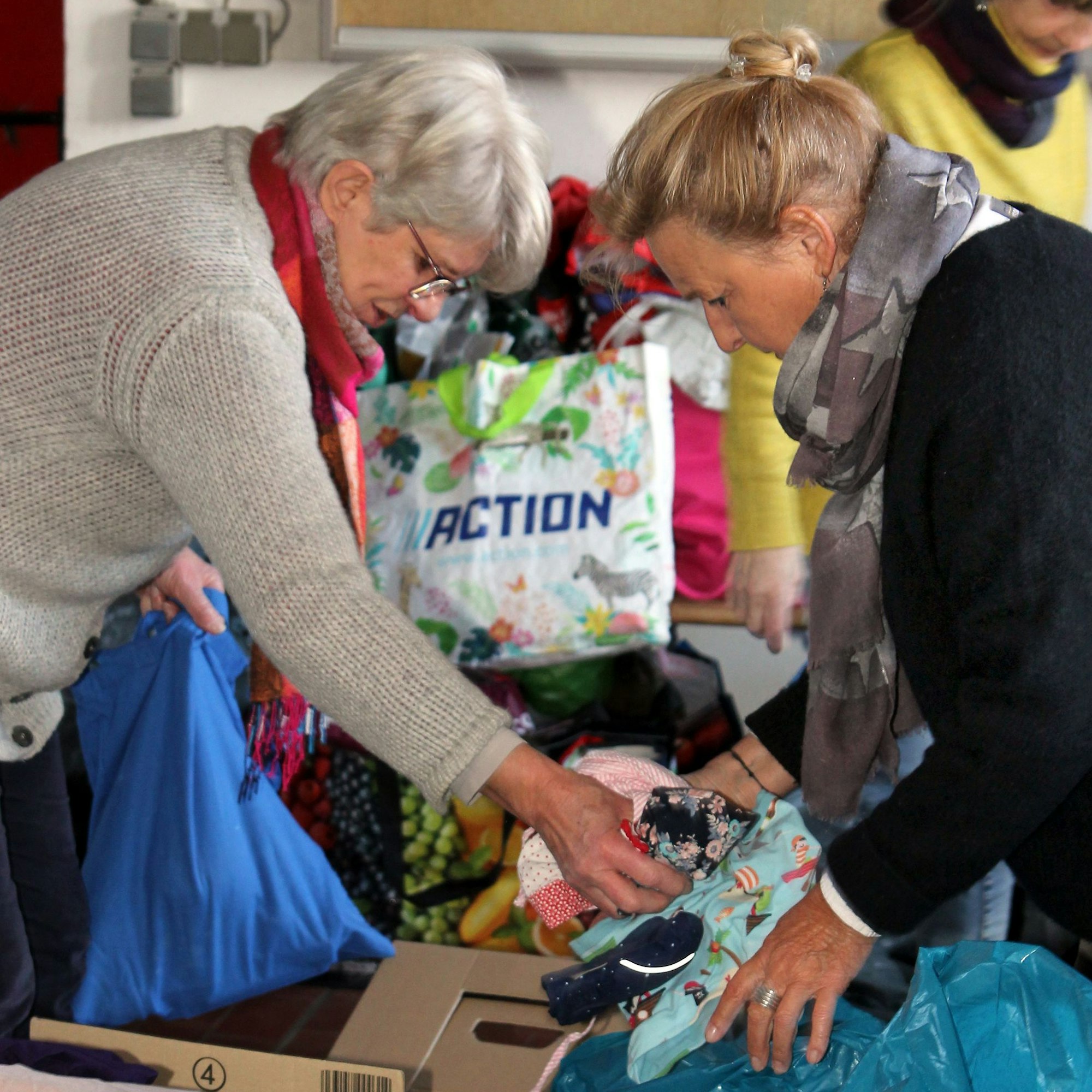 Zwei Frauen beugen sich über Kisten und sortieren Sachen.