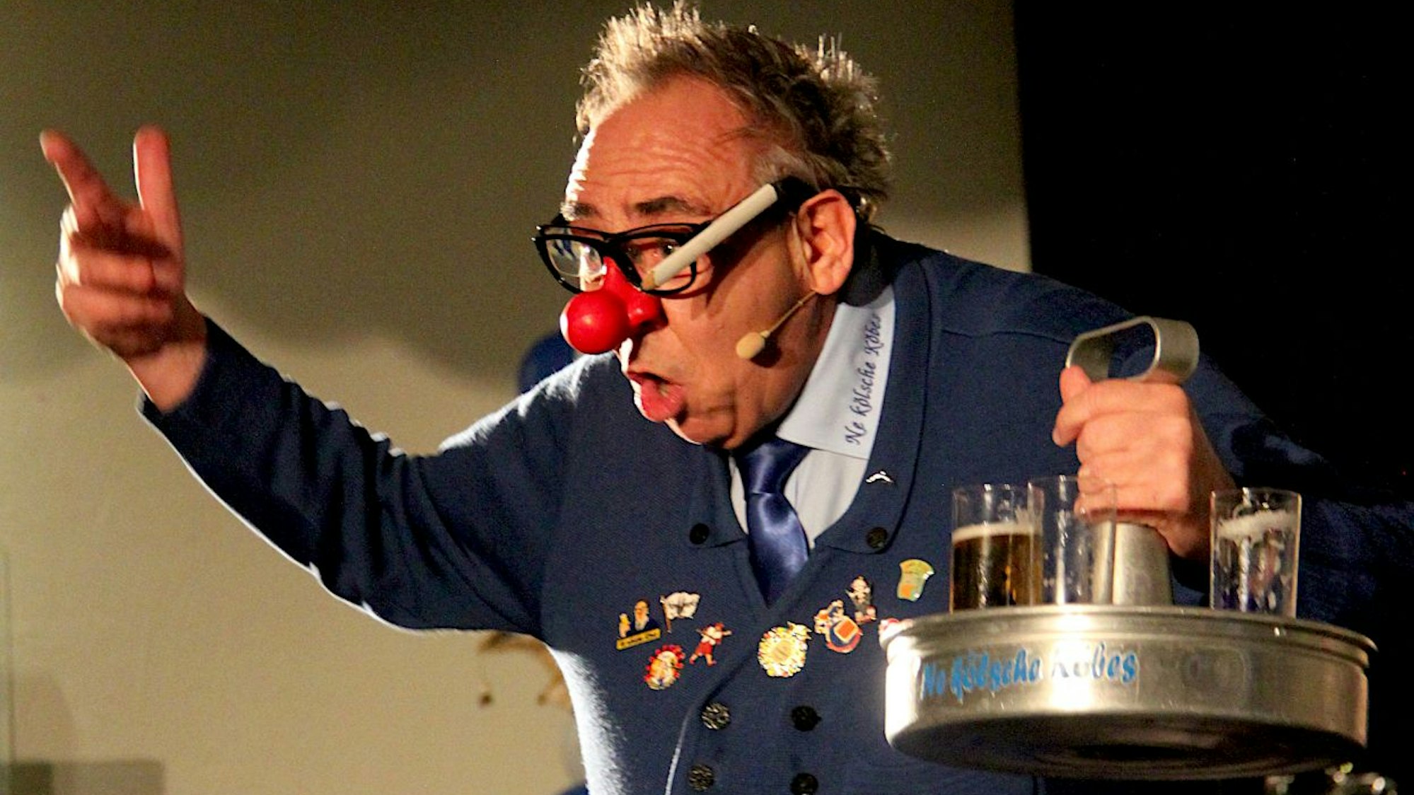 Karnevals-Redner mit roter Pappnase im Outfit eines kölschen Köbes mit einem Bierkranz in der Hand.