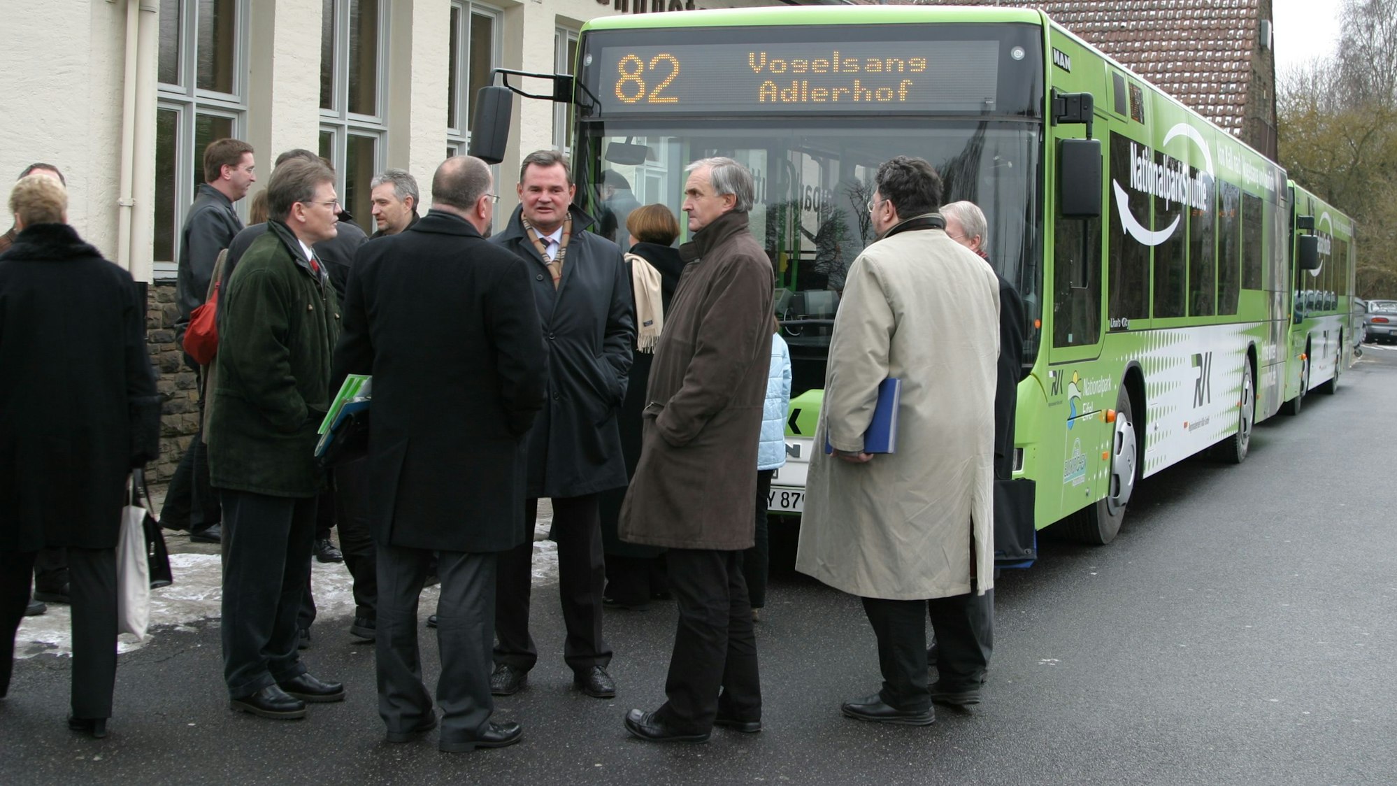 Am Bahnhof in Kall stehen mehrere Personen vor einem grünen Bus, dem Nationalparkshuttle.