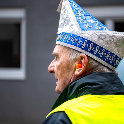 Ein Wagenengel mit Narrenkappe und gelber Warnweste trägt beim Karnevalszug einen Gehörschutz.
