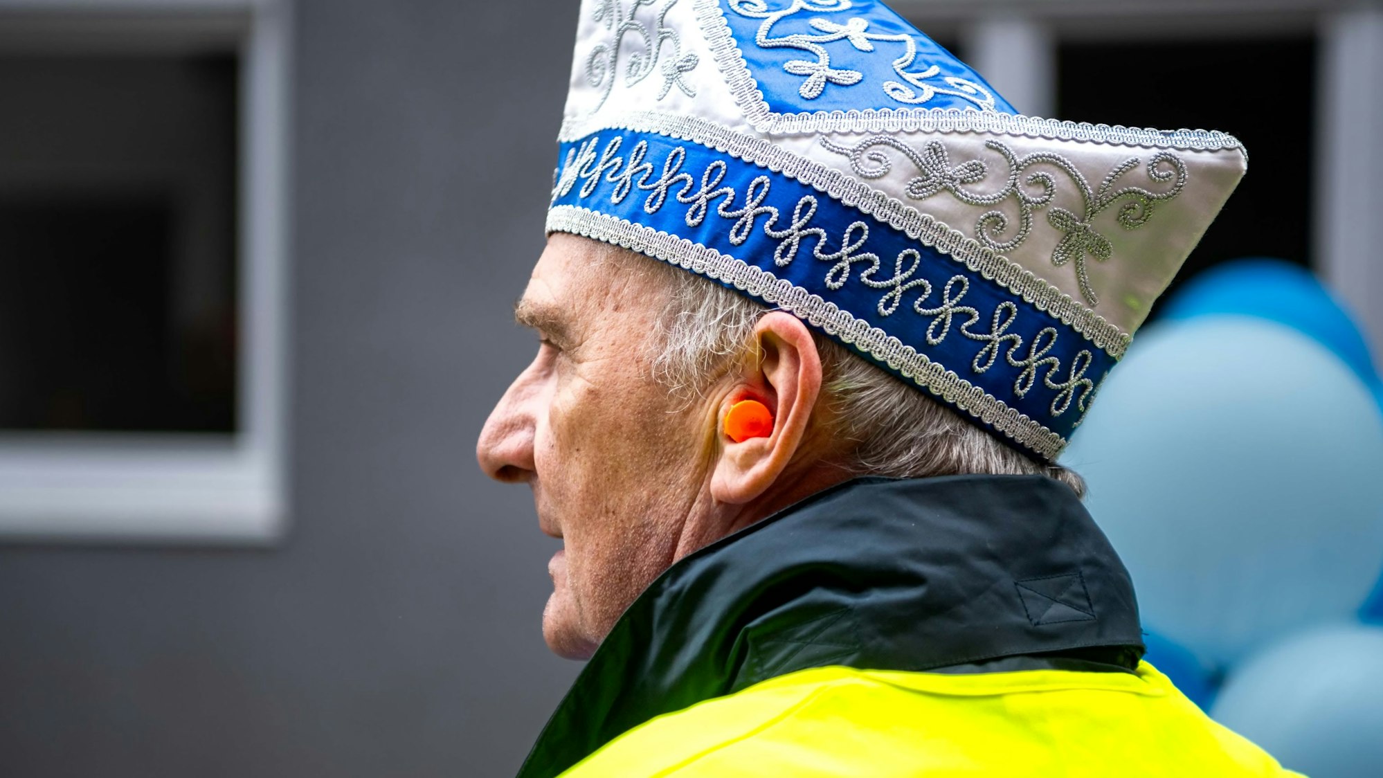 Ein Wagenengel mit Narrenkappe und gelber Warnweste trägt beim Karnevalszug einen Gehörschutz.