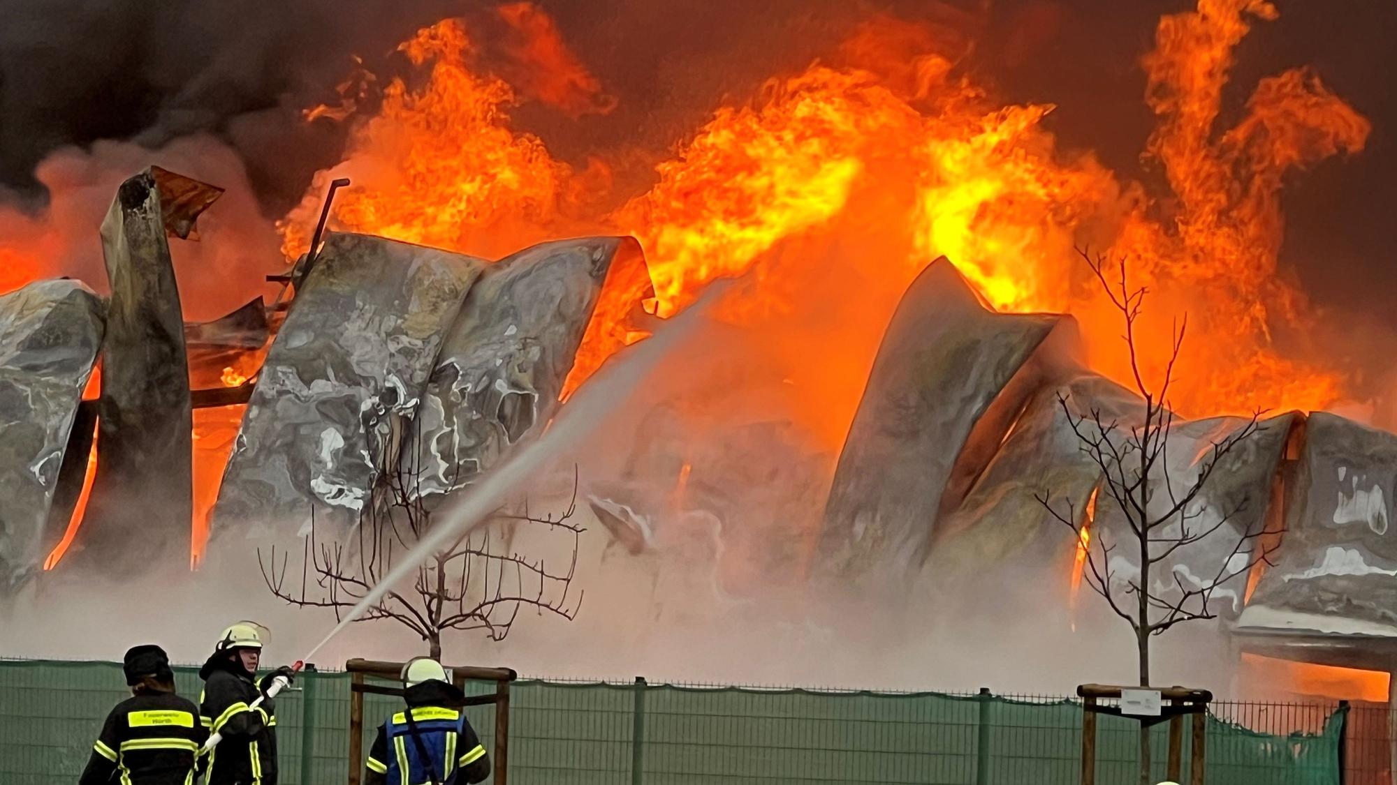Das Bild zeigt mehrere Feuerwehrleute vor einer brennenden Lagerhalle.