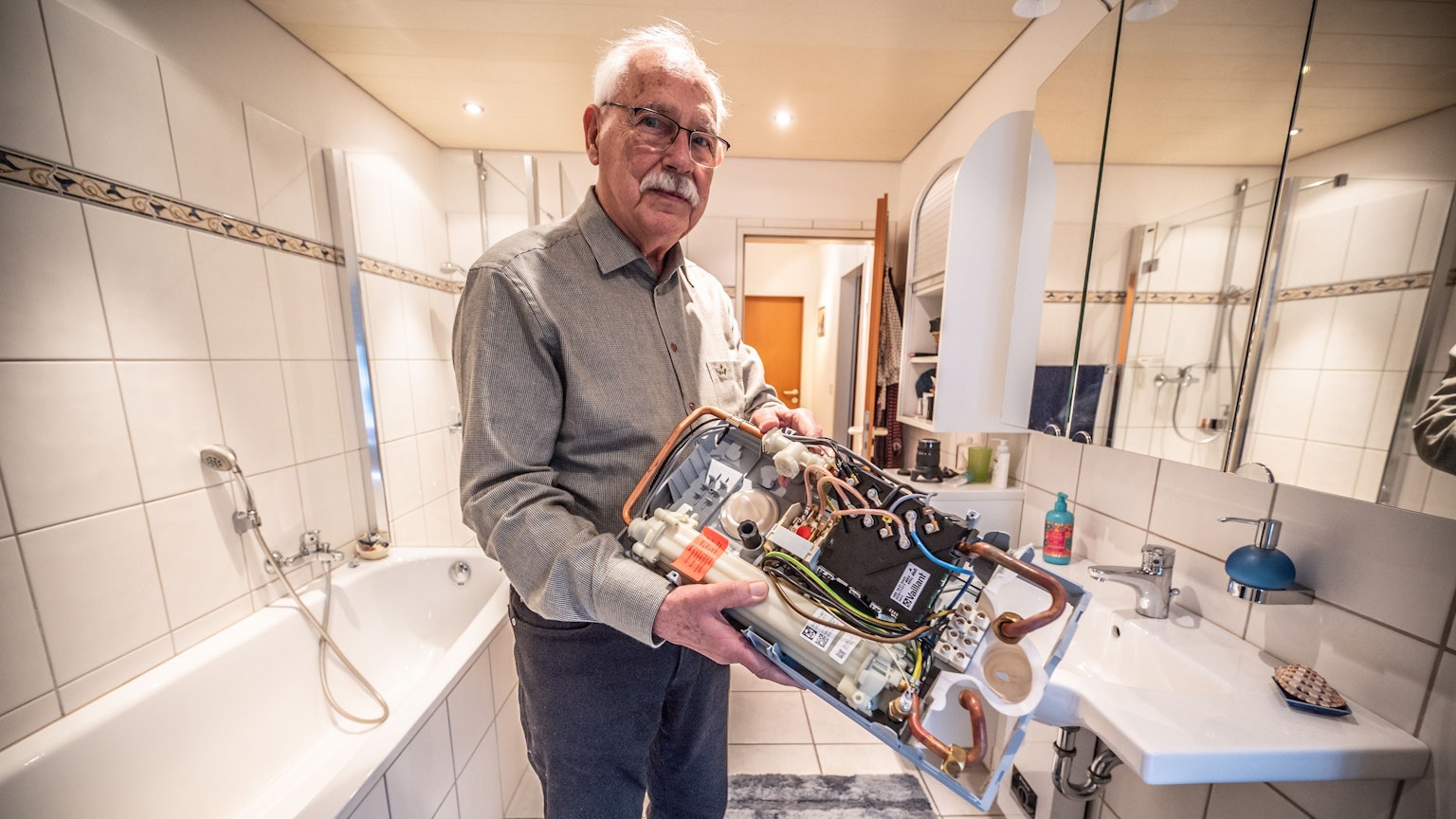 Harald Zander steht in seinem Bad mit dem defekten Durchlauferhitzer, dessen Elektronik am 11. Januar 2026 bei der mehrminütigen Überspannung abgeraucht war.