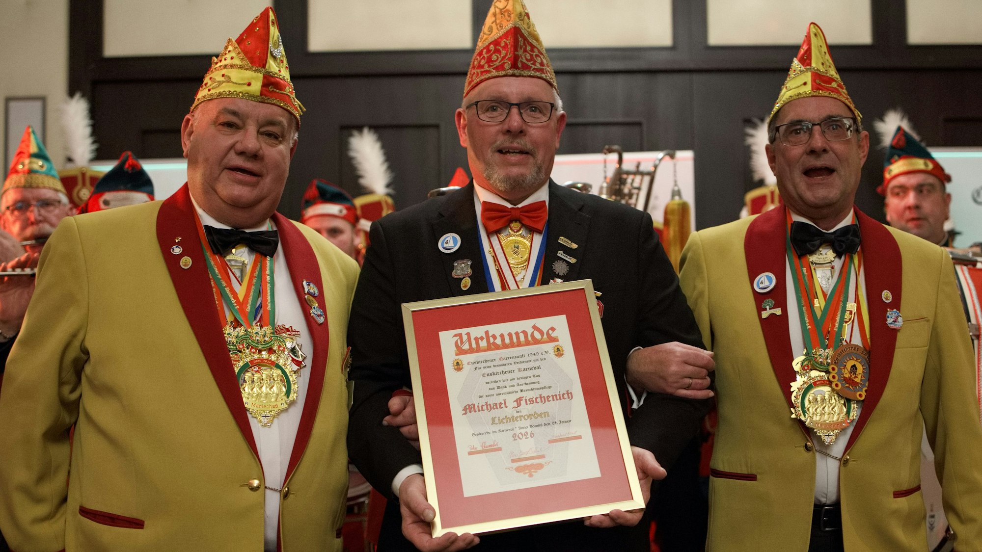 Michael Fischenich, der zwischen zwei Männern steht, die sich bei ihm eingehakt haben, hält eine Urkunde vor sich.