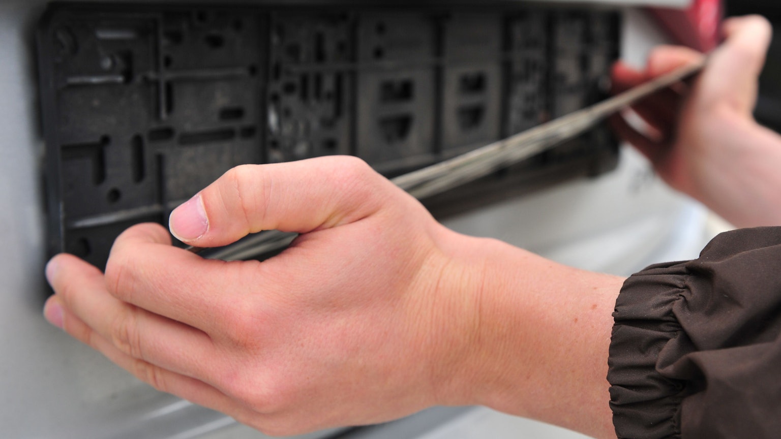 Das Foto zeigt zwei Hände, die nach einem Auto in einem Kennzeichenhalter greifen.