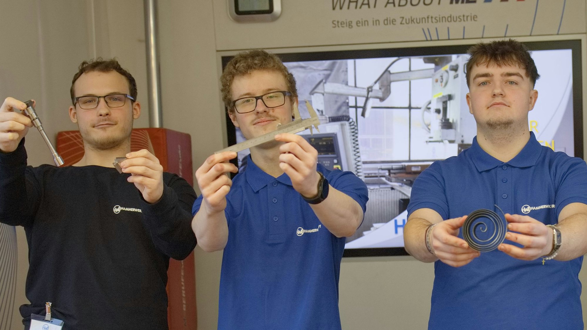 Drei junge Männer halten Werkzeuge und Materialstücke in den Händen. So zeigen sie, womit sie in ihren Berufen in der Metallindustrie arbeiten.