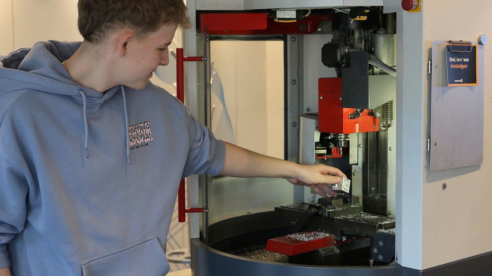 Ein Schüler steht an einer CNC-Fräsmaschine und setzt sie in Gang.