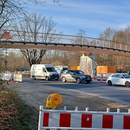 Eine nagelneue Rad- und Fußgängerbrücke aus Holz spannt sich über eine mehrspurige Straße.