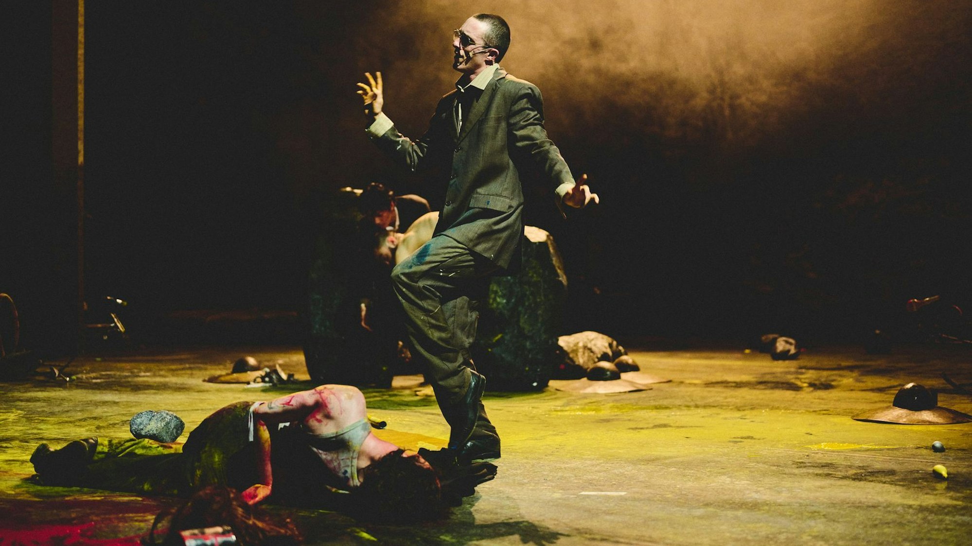 Ein Mann im Anzug tanzt. Vor und hinter ihm krümmen sich Männer am Boden.