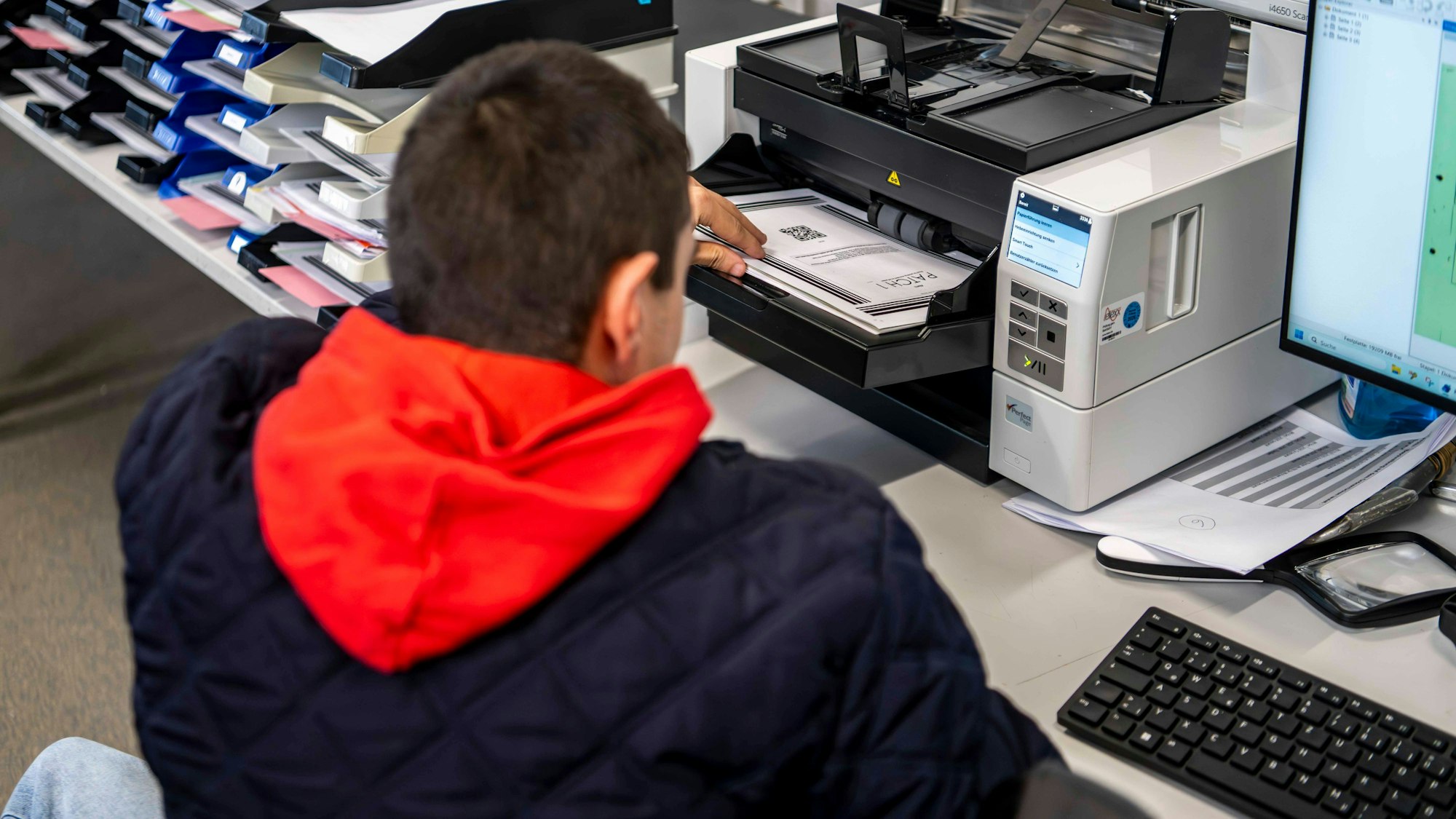 Das Bild zeigt einen Mitarbeiter der NEW, der Akten in den Scanner legt.