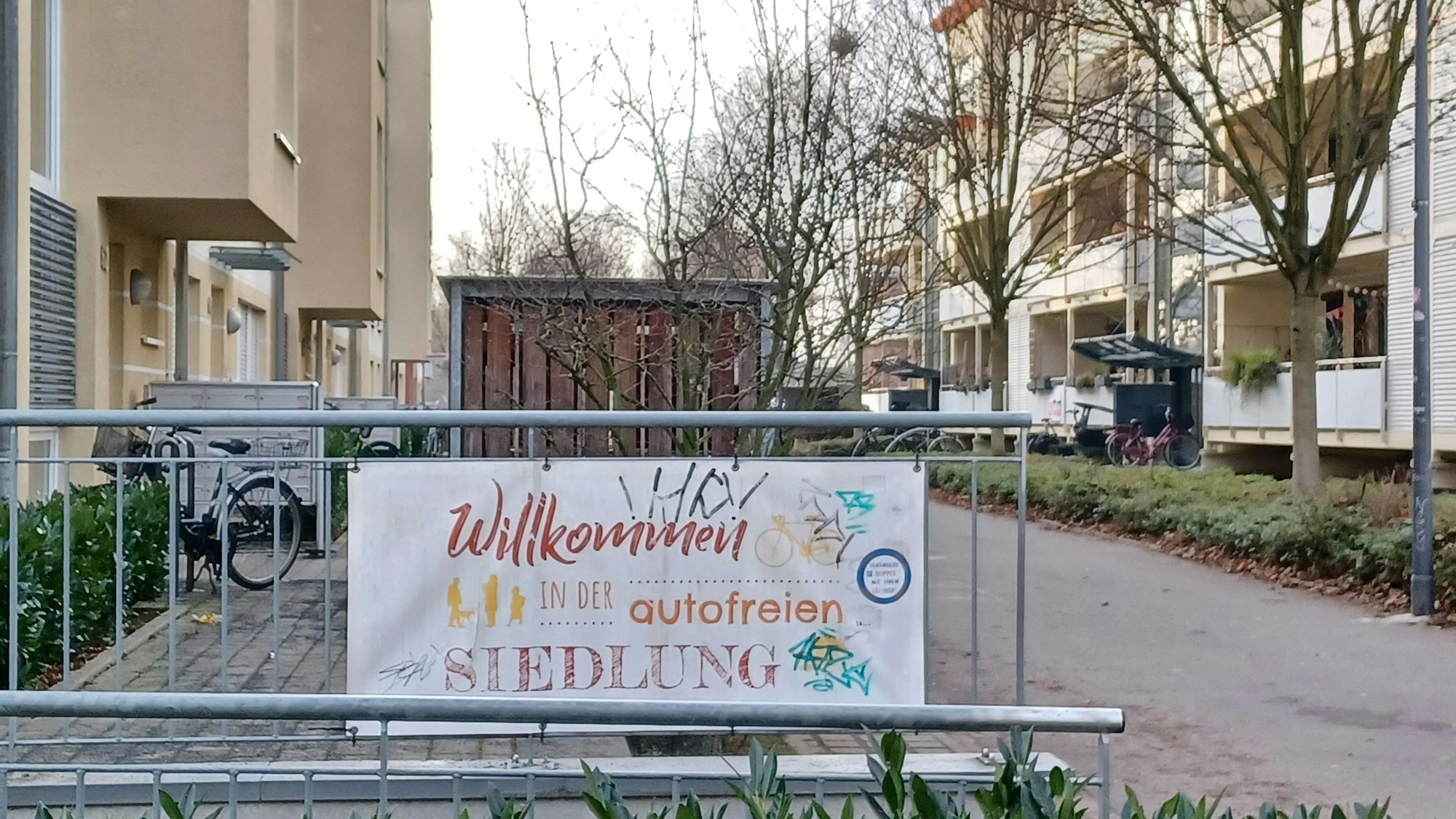 Ein Schild hängt an einem Gitter. Darauf steht „Willkommen in der autofreien Siedlung“.