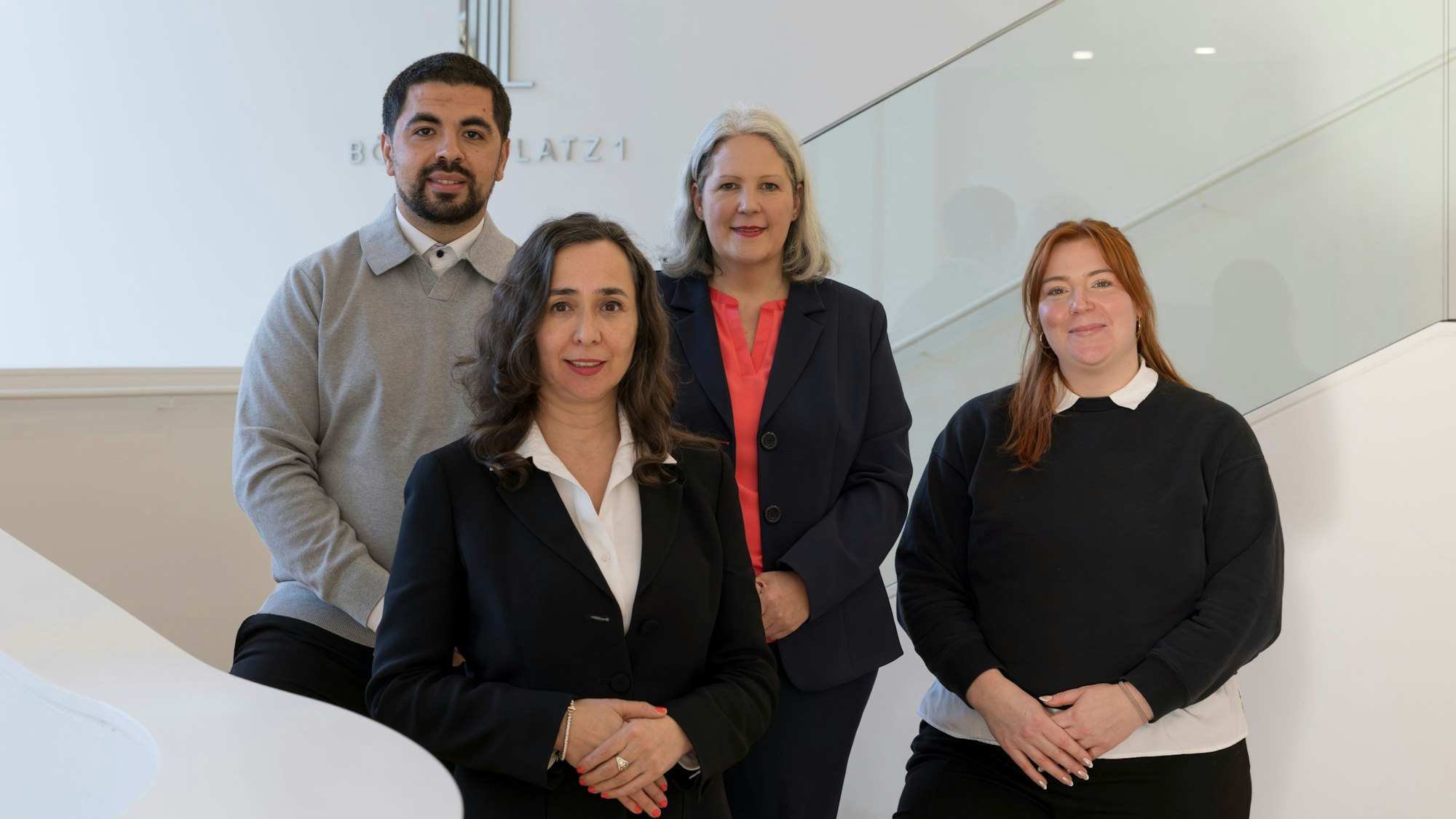 Vier Menschen stehen auf einer Treppe und schauen in die Kamera. Links ein Mann, rechts davon drei Frauen.