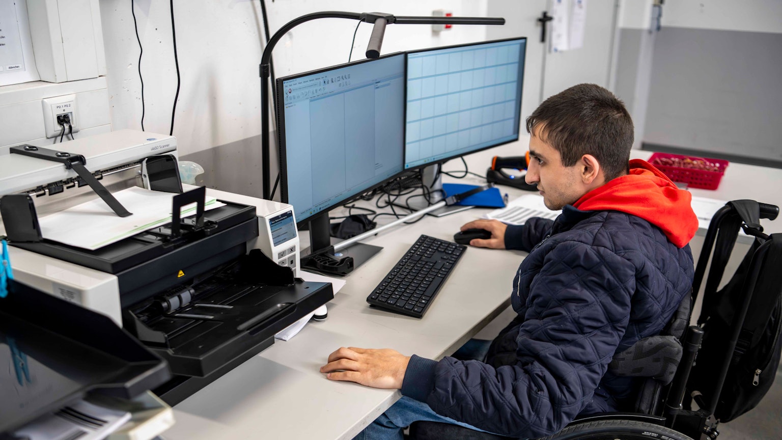 Das Bild zeigt einen Mitarbeiter der NEW, der vor einem Computer sitzt und Akten scannt.