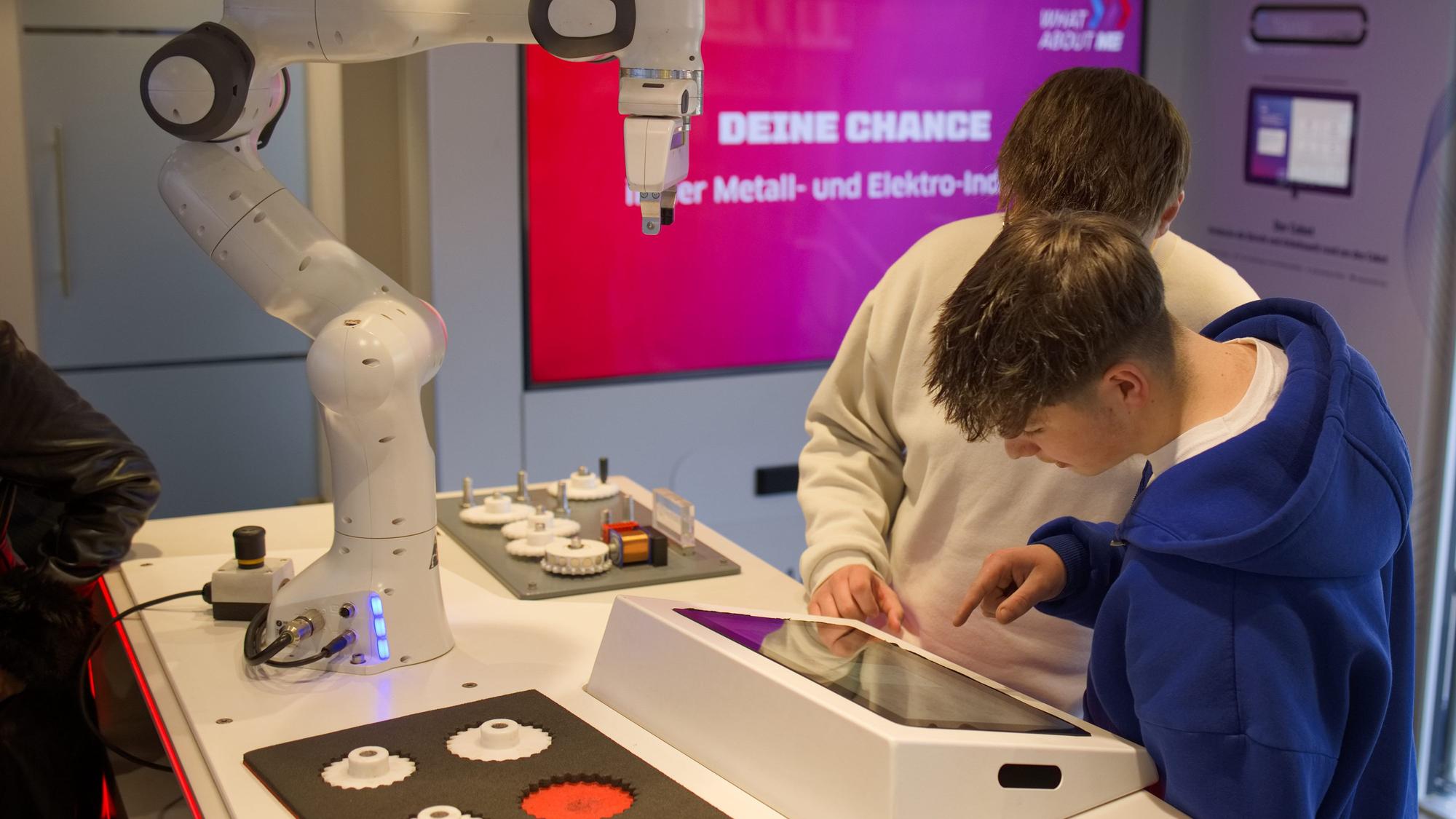 Im Infotruck des Arbeitgeberverbands Gesamtmetall stehen zwei Schüler an einem Roboter, den sie selbst steuern.