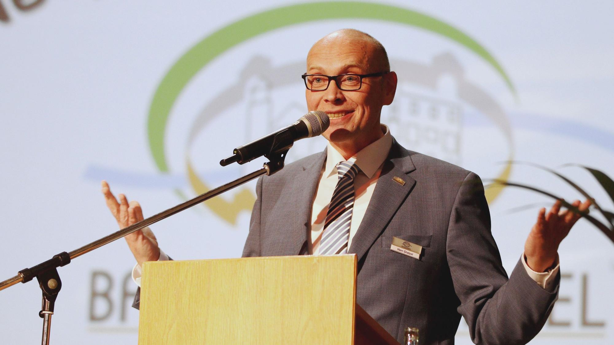 Bad Münstereifels Bürgermeister Sebastian Glatzel steht mit leicht ausgebreiteten Armen an einem Pult und spricht in ein Mikrofon.