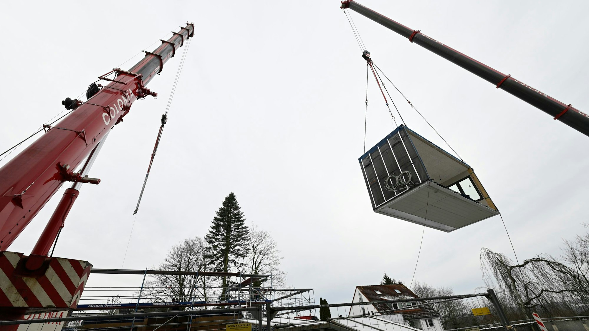 Ein Modul hängt am Haken eines Krans.Gegenüber steht ein zweiter Kran.