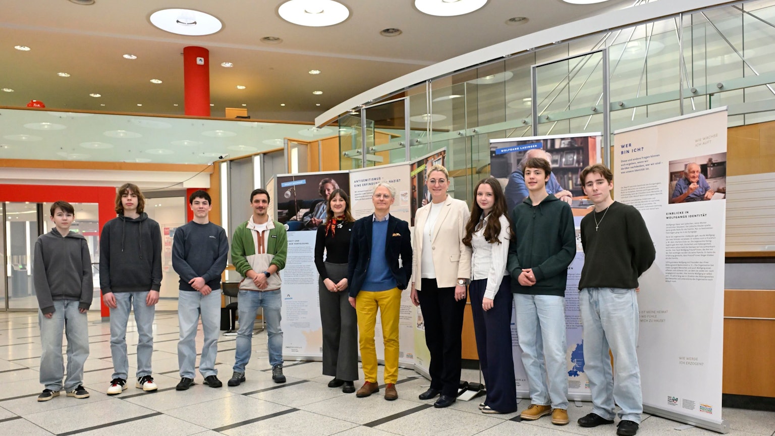 Eine Reihe von zehn Menschen steht im Eingangsbereich der Kreissparkasse Bergisch Gladbach vor Roll-ups, auf denen Texte und Fotos zu sehen sind.