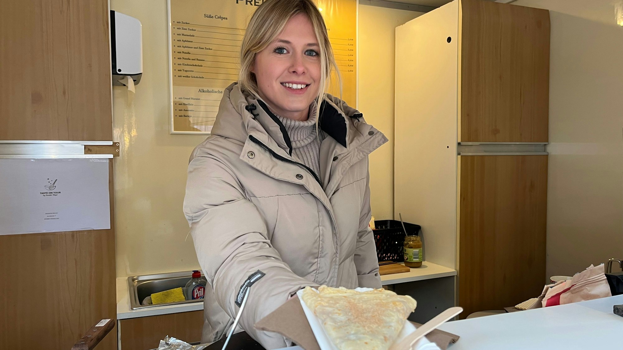 Das Foto zeigt eine junge Frau, die einen Crêpe reicht.