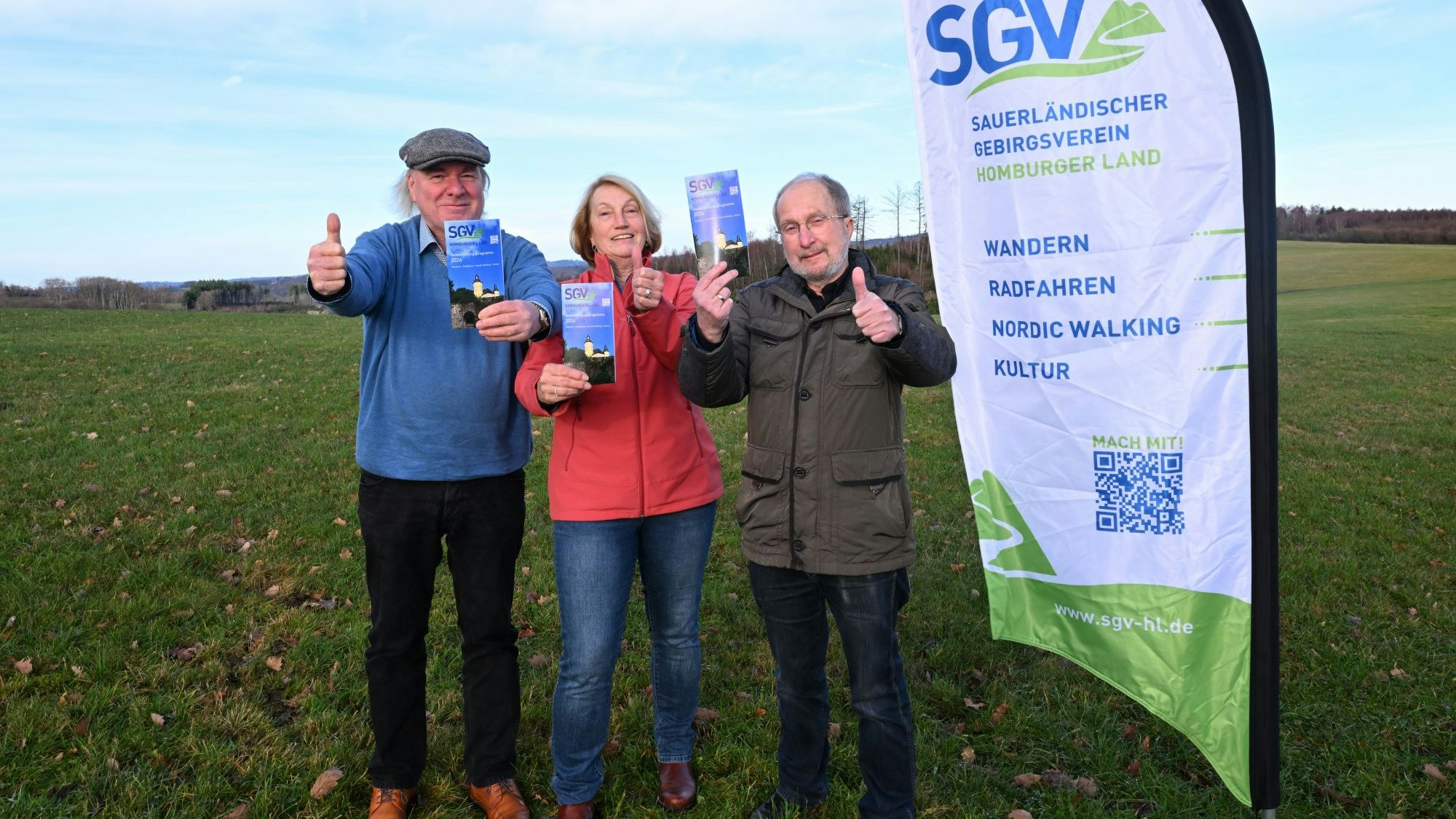 Zwei Männer und eine Frau halten Flyer in die Kamera.