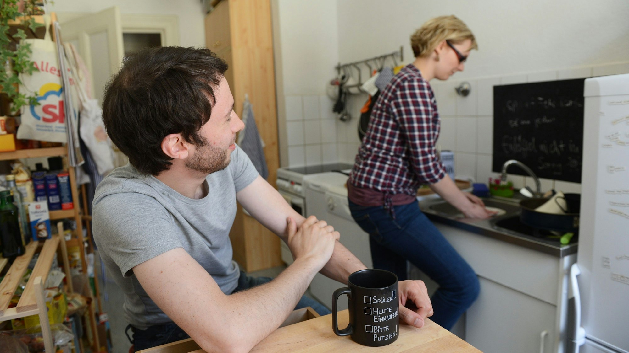 Ein Mann schaut zu, während eine Frau den Abwasch erledigt. 28 Prozent der Befragten sehnen sich nach traditionellen Rollenbildern, das zeigt die repräsentative „Next-Generation“-Studie der Allianz-Foundation. (Symbolbild)