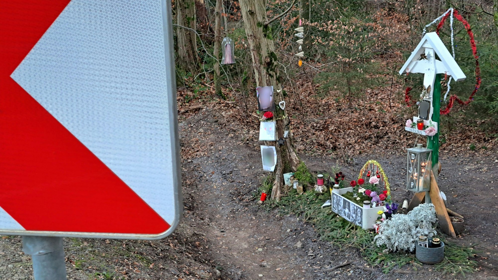 Neben einer Straße mit rot-weißen Warntafeln in einer Kurve steht ein Kreuz, das an einen tödlichen Unfall erinnert.