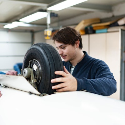 Zu sehen sind zwei Personen, die am Rad eines Segelflugzeugs beschäftigt sind.
