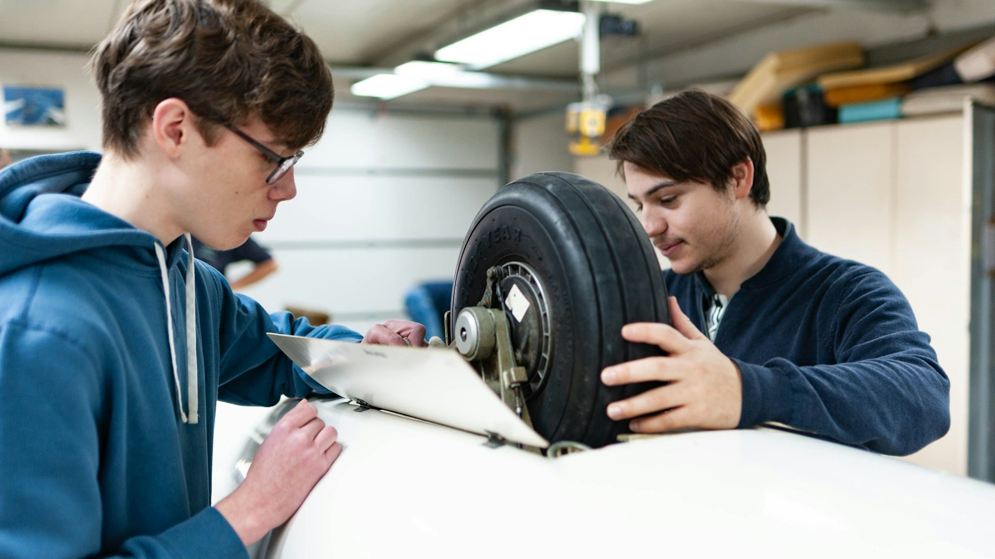 Zu sehen sind zwei Personen, die am Rad eines Segelflugzeugs beschäftigt sind.