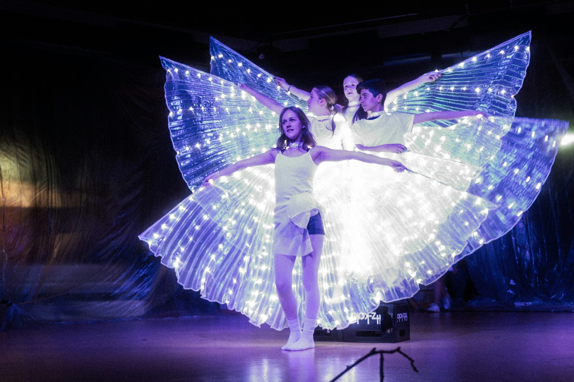 Drei Mädchen mit leuchtenden Flügeln stehen hintereinander auf einer Theater-Bühne.