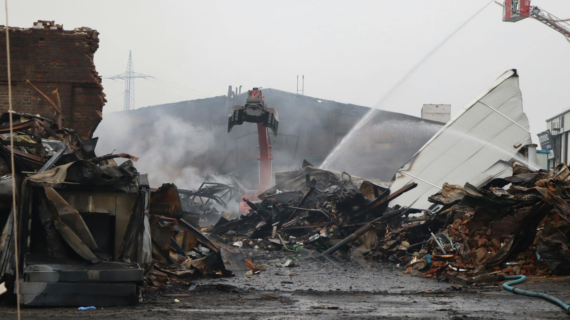 Ein Bagger steht inmitten von Trümmern, auch Wasserfontänen sind zu sehen.