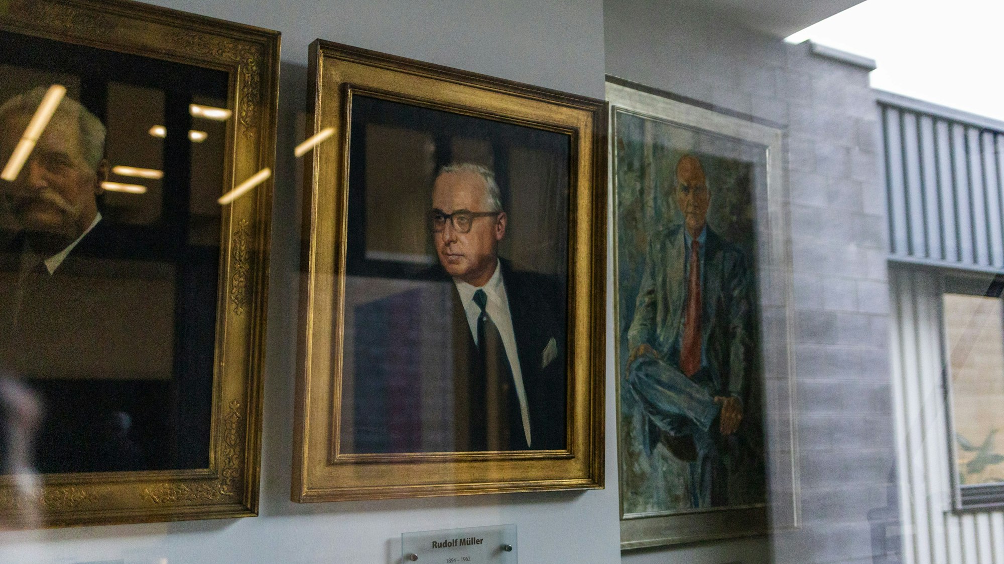 Drei Ölgemälde mit älteren Männern darauf hinter einer Glasscheibe.