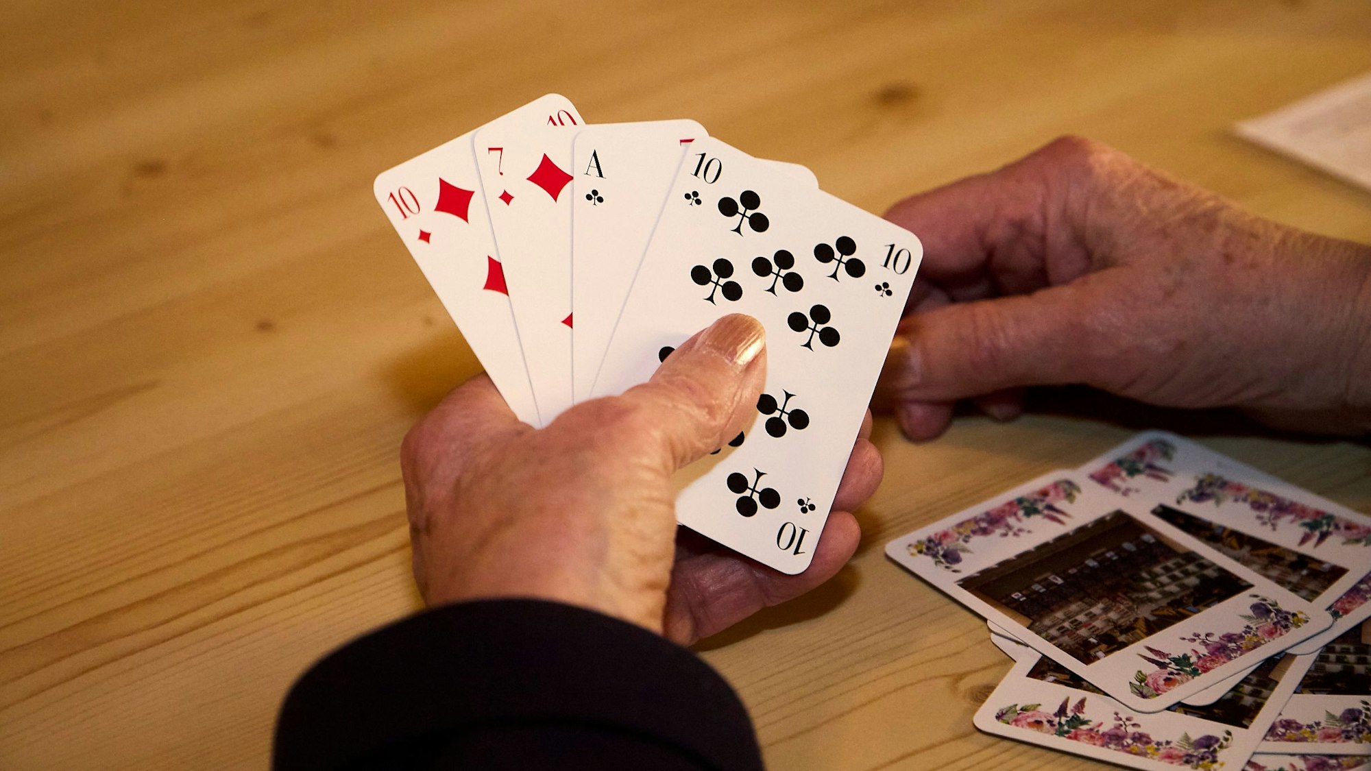 Nahaufnahme auf eine Hand, die auf einem Holztisch ruht und vier Karten hält