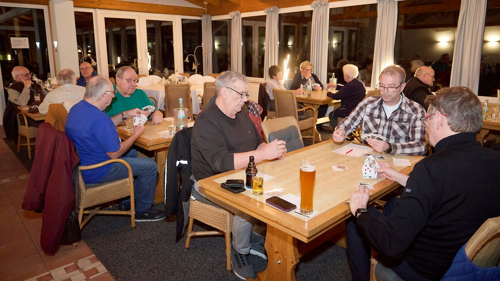 Mehrere Trios sitzen an Tischen und Spielen Skat.